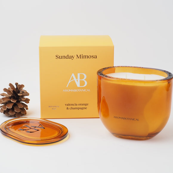 Aromabotanical - Sunday Mimosa luxury scented candle in an elegant Amber glass vessel with matching lid. Featuring a Valencia Orange and Champagne fragrance 400g